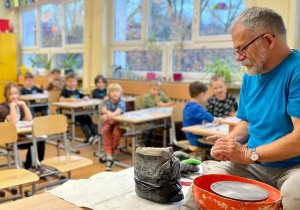 Prowadzący uciął kawałek gliny z dużego kawałka, aby pokazać dzieciom elastyczność gliny.