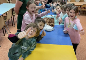 Uczniowie razem z panią Marianną zapozowali do wspólnego zdjęcia stojąc dookoła stołu przy którym będą dekorować pierniczki. Wszyscy są uśmiechnięci.