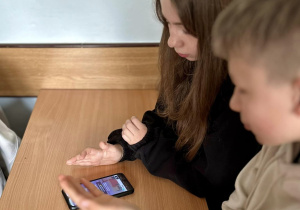 Idalia z Adamem patrzą na telefon czekając na potwierdzenie, czy ich odpowiedź jest prawidłowa.
