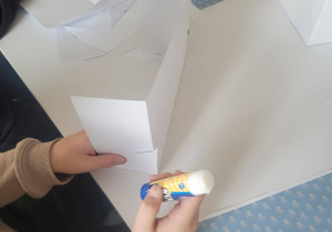 Uczeń skleja wycięte elementy papieru.