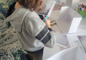 Dziewczynka stoi przy stole i wycina kawałek papieru potrzebny do projektu mieszkania.