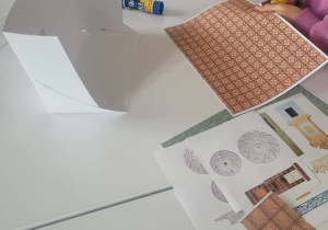 Dziewczynka stoi przy stole i wycina kawałek papieru potrzebny do projektu mieszkania.