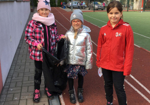 Kasia, Ania i Oliwia z workiem na śmieci zaczynają sprzątanie boiska.
