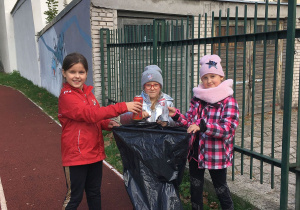 Oliwia, Ania i Kasia wrzucają do worka pierwsze śmieci.