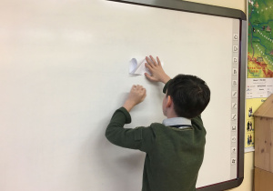 Adam pokazuje na tablicy krok po kroku, jak składać papier.