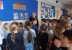 Uczniwie podczas spaceru po szkole, stoją pod tablicą dekoracyjną, ogladaja zdjęcia i słuchają nt historii związanej z odzyskaniem Niepodległości.