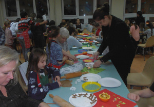 Rodzice z dziećmi, przy świątecznie udekorowanym stole, przygotowują ciasto na pierniki.