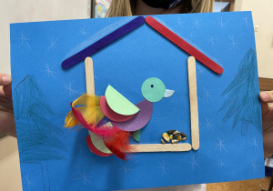 Uczennica prezentuje swoją pracę - Ptaszek z kółek origami w karmniku.