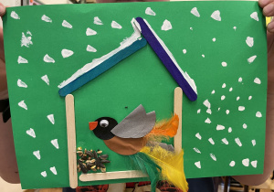 Uczeń prezentuje swoją pracę - Ptaszek z kółek origami i piórek w karmniku.