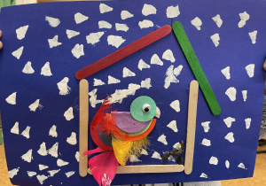 Uczennica prezentuje swoją pracę - Ptaszek z kółek origami i piórek w karmniku.