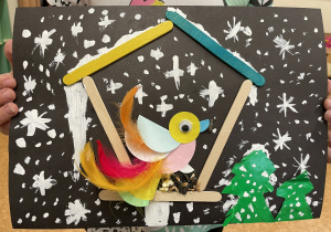 Uczennica prezentuje swoją pracę - Ptaszek z kółek origami i piórek w karmniku.