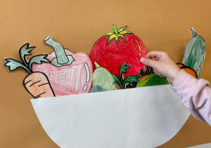 Uczeń wkłada wyciętego pomidora do misi przyczepionej do tablicy.