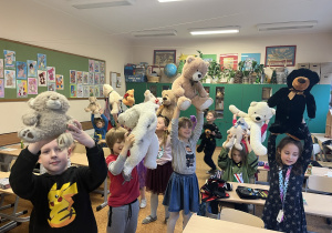 Dzieci prezentują swoje misie unosząc je do góry nad głowami.
