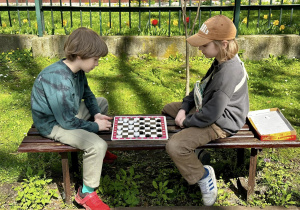 Julian i Kajtek, siedząc na ławce, grają w warcaby.
