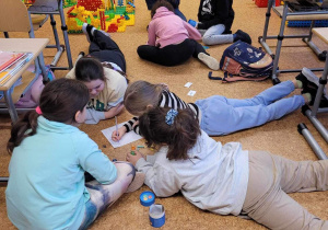 Uczniowie w grupkach siedząc i leżąc na podłodze tworzą opowiadania.