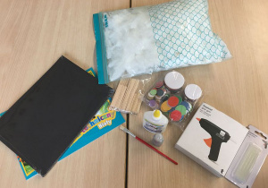 Różnorodne materiały do wykonania pracy (kartki A4 - białe i czarne, białe piórka, patyczki drewniane, klej magiczny, papier do origami - kółka, pestki słonecznika).
