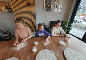 Hanna, Gabriela i Ola przygotowują swoje kawałki ciasta do pizzy.