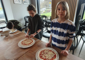Scarlett i Przemysław dosypują sera do pizzy.