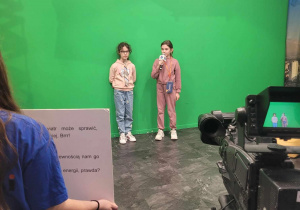 Julia i Ewa w roli prowadzących program telewizyjny stoją przed kamerami na zielonym tle.