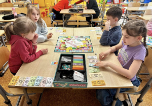 Uczniowie siedzą przy stolikach i grają w gry.