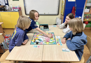 Uczniowie siedzą przy stoliku i grają w Monopoly Squishmallows.