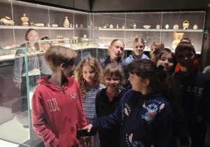 Uczniowie stoją w sali muzealnej między szklanymi gablotami.