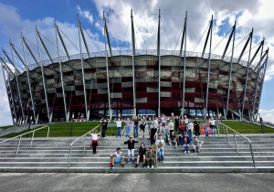 Uczniowie stoją na schodach pozując do grupowego zdjęcia. W tle widać Stadion Narodowy.