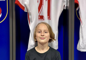 Ignacy siedzi na ławce w szatni i pozuje do zdjęcia pod koszulką piłkarza o nazwisku Zalewski.
