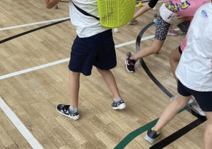 Uczniwoie podcza gry ruchowej zbierają kolorowe piłeczki do plastikowych koszyczków.