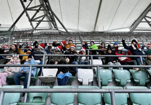 Uczniowie siedzą na trybunie stadionu i słuchają historii klubu.