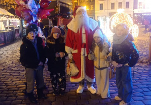 Uczniowie znajdują się na rynku miasta i pozują z Mikołajem do grupowego zdjęcia.