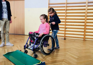 Uczennice z zerówki podczas pokonywania przeszkody wózkiem inwalidzkim.
