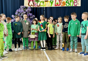 Klasa 1a, ubrana w zielone kolory, wita wiosnę wierszem.