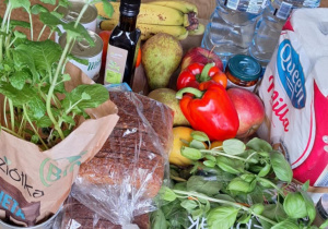 Produkty spożywcze, które zakupili rodzice uczniów. Na ławce widać świeżą miętę, chleb razowy, sałatę, owoce, warzywa i wodę.