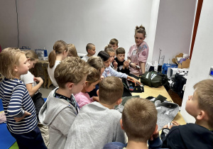 Uczniowie znajdują się w Strefie Szycia, stoją wokół stołu krawieckiego i oglądają materiały.