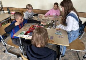 Uczniowie z klas 3a i 3b siedzą przy stoliku i grają w Monopoly.