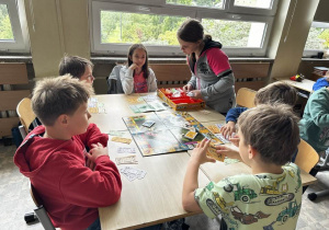 Uczniowie z klas 3a i 3b siedzą przy stoliku i grają w Monopoly.