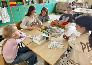 Uczniowie z klas 3a i 3b siedzą przy stoliku i grają w Monopoly.
