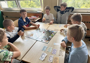 Uczniowie z klas 3a i 3b siedzą przy stoliku i grają w Monopoly.