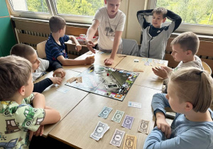 Uczniowie z klas 3a i 3b siedzą przy stoliku i grają w Monopoly.