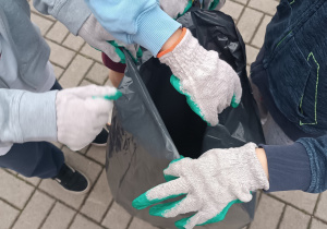 Uczniowie zebrane śmieci wkładają do worków.