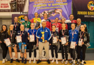 Reprezentacja Mazowsza stoi przy podium podczas dekoracji medalami. Trener trzyma w rękach puchar, a zawodniczki - dyplomy.