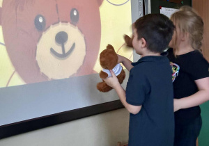 Uczniowie tańczą ze swoimi misiami do piosenki oglądając filmik edukacyjny "Jak narysować Misia?".