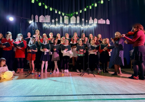 Chór śpiewa świateczną piosenkę. Pani Olga i uczennica grają na skrzypcach.