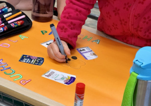 Dziewczynka koloruje na czarno psią łapkę, którą naszkicowała na plakacie.