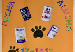 Plakat "Pucha dla Palucha" na pomarańczowym kartonie, z kolorowymi literami i cyframi oraz kolorowankami przedstawiającymi puszki z karmą dla psów.