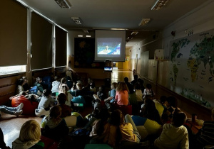 Uczniowie siedzą lub leżą na pufach na korytarzu i oglądają bajkę "Zakochany Kundel".