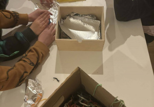 Dzieci, siedząc przy stoliku, wykonują zabawkę "Zośkę".