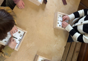 Dziewczynki, siedząc przy stole, wykonują zegary z drewna.