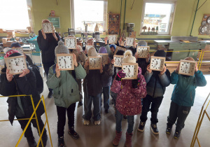 Dzieci, stojąc w nowoczesnej stolarni, prezentują swoje zegary.